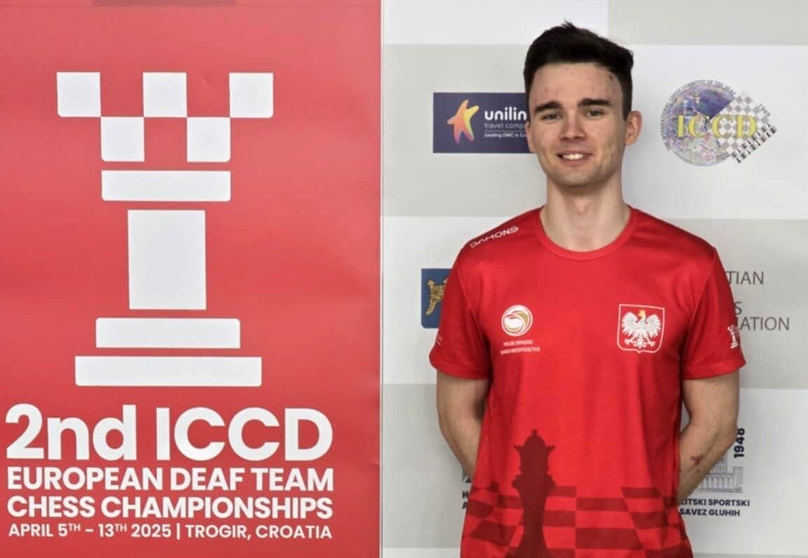 Mężczyzna w czerwonej koszuli stoi obok szachownicy