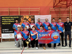 Drużyna koszykówki mężczyzn składa się z jedenastu zawodników i jednego trenera. Wszyscy ubrani są w niebiesko-czerwone stroje sportowe i mają na szyjach medale. Pośrodku stoi duży złoty puchar. Za nimi widać transparenty z napisami "MISTRZOSTWA POLSKI NIESŁYSZĄCYCH W KOSZYKÓWCE MĘŻCZYZN", "GLIWICE 16-18.05.2025" oraz "ŚWIT WROCŁAW".